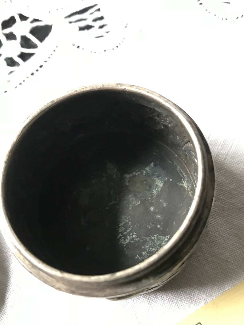 May include: A silver, round, decorative box with a slightly tarnished interior. The box has a textured, embossed design on the exterior.