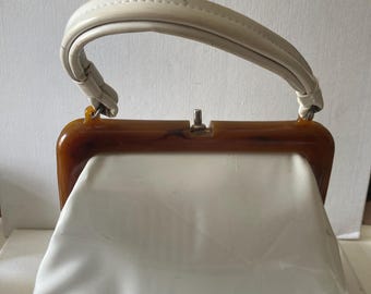 Puede incluir: Bolso de mano blanco vintage con asa color crema y marco efecto carey. El bolso tiene cierre de broche y un diseño estructurado. Un accesorio clásico para llevar lo esencial.