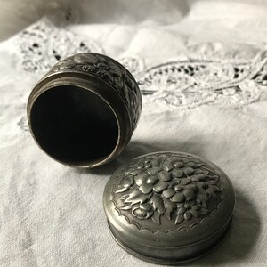 May include: A silver trinket box with an ornate floral design. The box is open, revealing the empty interior.