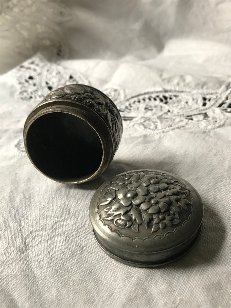 May include: A silver trinket box with an ornate floral design. The box is open, revealing the empty interior.