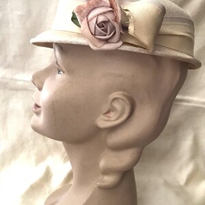May include: A white straw hat with a pink fabric rose and a white satin bow. The hat is on a mannequin head.
