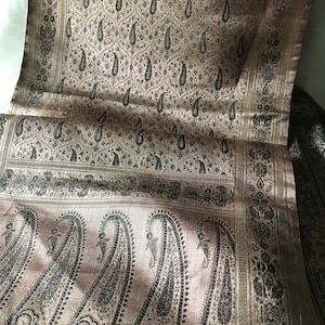 May include: A brown and black paisley patterned fabric with a satin sheen. The fabric has a repeating pattern of paisley shapes and small floral designs.