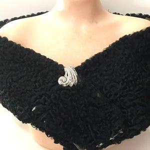 May include: A black fur shawl with a silver brooch. The shawl is made of a soft, fluffy material and has a simple, elegant design.