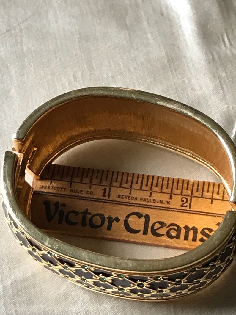 以下が含まれることがあります： 黒と緑のエナメル模様の金製のバングルブレスレット。ブレスレットは小さな緑色の石で飾られています。ブレスレットの直径は約5cmです。