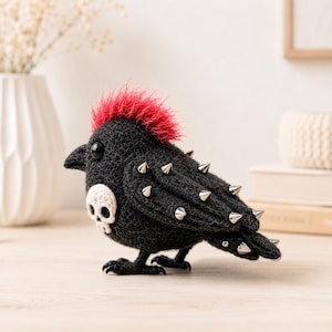 May include: A black bird figurine crafted from textured material, featuring a vibrant red mohawk, a white skull appliqué on its chest, and silver-toned metal spikes embedded along its wing and tail feathers. The bird has a dark beak and eyes.