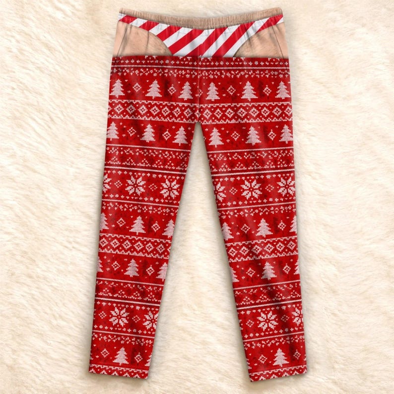 May include: Red leggings featuring a white fair isle pattern of Christmas trees and snowflakes. The waistband area displays a printed graphic of skin-toned fabric with a red and white diagonal striped thong design visible at the top edge.