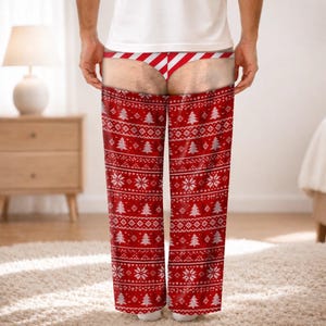 May include: Red and white lounge trousers featuring a festive holiday pattern of Christmas trees and snowflakes. The design includes a printed graphic of a red and white striped thong at the waistline, creating an illusion of exposed skin.