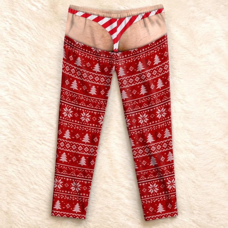May include: Red leggings featuring a white Nordic-style pattern of snowflakes and Christmas trees. The upper section displays a graphic print of skin-toned buttocks wearing a red and white striped thong, creating a humorous visual illusion.