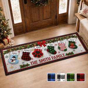May include: A rectangular Christmas-themed floor mat featuring a white quilted background with a red and black plaid border. The mat displays a garland with six hanging stockings labeled Daniel, Sophia, Buddy, Liam, Emily, and Jacob. The text THE SMITH FAMILY is printed in red. A paw print stocking is centered.