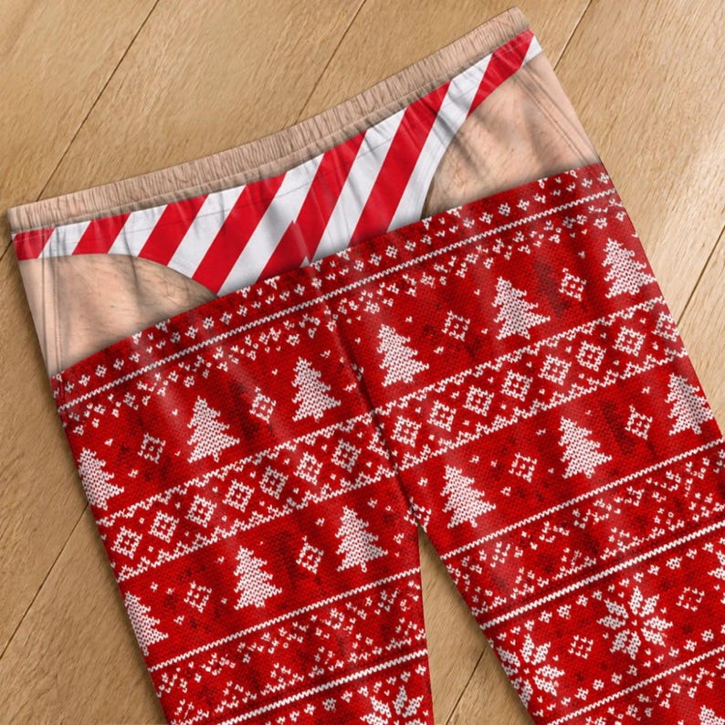 May include: Leggings featuring a red and white knit-style pattern with Christmas trees and snowflakes. The waistband area displays a printed graphic of skin-toned fabric and a red and white diagonal striped thong-style undergarment design.
