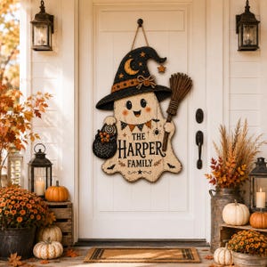 May include: A wooden door sign shaped like a ghost wearing a black witch hat with a crescent moon and stars. The ghost holds a broom and a basket of candy, featuring the text THE HARPER FAMILY in black lettering with orange and black accents.