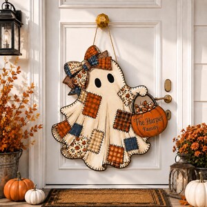 Peut inclure: Une décoration de porte en forme de fantôme avec un motif patchwork de carreaux et de fleurs orange, bleu et crème. Le fantôme porte un grand nœud assorti et tient un seau citrouille orange avec le texte The Harper Family imprimé dessus.