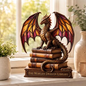 May include: A bronze-colored dragon figurine with stained-glass style wings in orange and purple, perched atop a stack of four books. The base book features the text "THE MORGAN DRAGON LIBRARY" and "EST. 2025" engraved on the front edge.