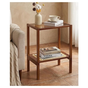 May include: A rectangular wooden side table with a brown finish, featuring a top surface and a lower shelf with a yellow woven rattan inlay. The table holds a white vase with dried flowers, a white teacup on a saucer, and two stacked books.