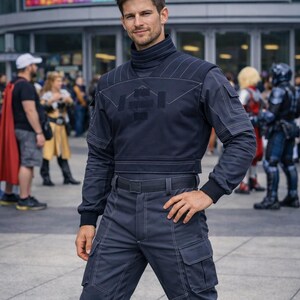 May include: A dark navy blue tactical uniform consisting of a long-sleeved mock neck top with white contrast stitching and a geometric chest patch, paired with matching cargo trousers featuring a belt and multiple utility pockets on the legs.