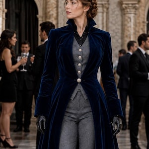 May include: A floor-length navy blue velvet coat with a high collar and a single button closure, worn over a grey waistcoat with silver buttons, a black collared shirt, grey trousers, and black lace-up boots, accessorised with black leather gloves.