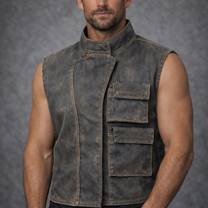 May include: A sleeveless vest in a distressed charcoal gray finish featuring a high collar, an asymmetrical front closure, and two stacked rectangular cargo pockets on the left side. The garment has visible stitching and a weathered, textured appearance.
