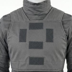 Op de afbeelding: Een grijze tactische vest met een hoge kraag en meerdere klittenband patches. De vest is gemaakt van een duurzame stof en heeft versterkte stiksels. Het ontwerp suggereert bescherming en functionaliteit, geschikt voor diverse toepassingen.