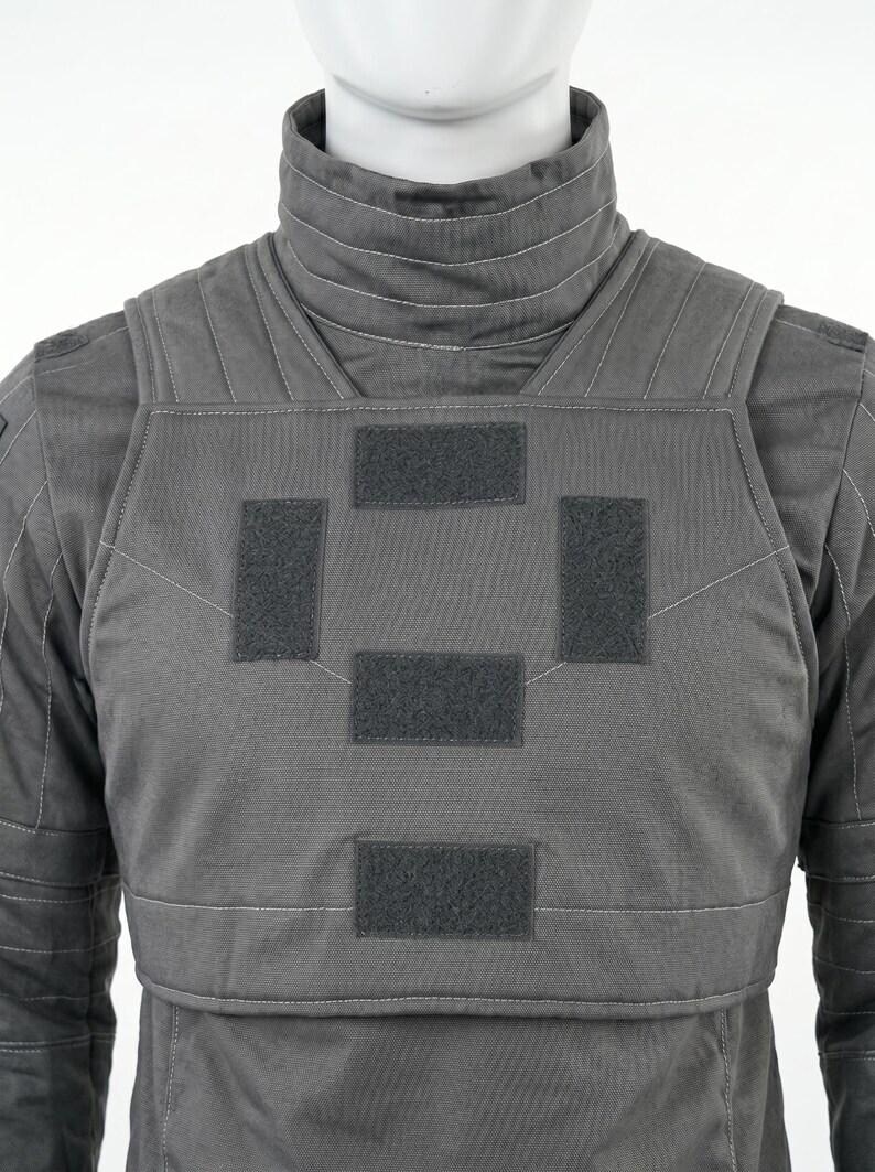 Op de afbeelding: Een grijze tactische vest met een hoge kraag en meerdere klittenband patches. De vest is gemaakt van een duurzame stof en heeft versterkte stiksels. Het ontwerp suggereert bescherming en functionaliteit, geschikt voor diverse toepassingen.