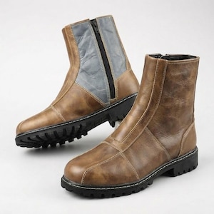 K&ouml;nnte beinhalten: Ein Paar Stiefeletten mit brauner, strukturierter Oberfl&auml;che und schwarzer Profilsohle. Ein Stiefel hat einen seitlichen Rei&szlig;verschluss und einen grauen Kontrasteinsatz am Schaft, w&auml;hrend der andere eine braune Vorderseite mit sichtbaren N&auml;hten zeigt.