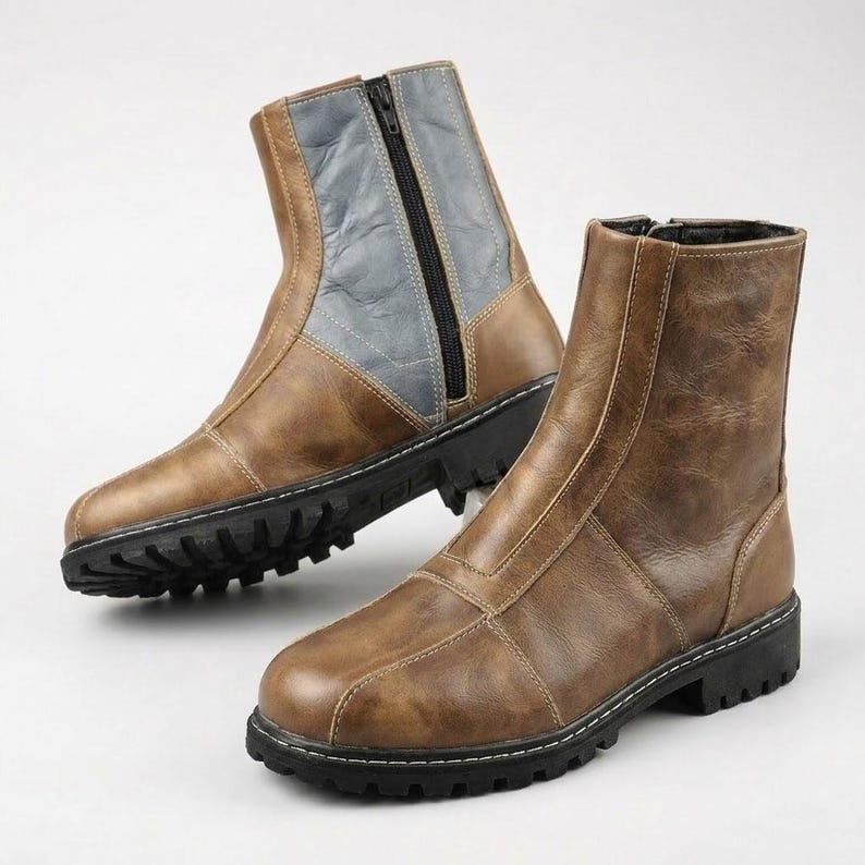 K&ouml;nnte beinhalten: Ein Paar Stiefeletten mit brauner, strukturierter Oberfl&auml;che und schwarzer Profilsohle. Ein Stiefel hat einen seitlichen Rei&szlig;verschluss und einen grauen Kontrasteinsatz am Schaft, w&auml;hrend der andere eine braune Vorderseite mit sichtbaren N&auml;hten zeigt.