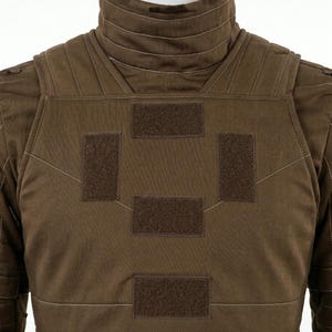 K&ouml;nnte beinhalten: Eine braune taktische Weste mit hohem Kragen und horizontalen N&auml;hten, strukturierten Schulterpartien und vier rechteckigen Klettverschluss-Patches auf der Brust. Das Kleidungsst&uuml;ck ist mit sichtbaren N&auml;hten verarbeitet.