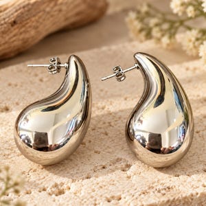 May include: A pair of silver-toned teardrop-shaped stud earrings with a smooth, highly reflective polished finish. Each earring features a curved, bulbous design that tapers to a point at the top, secured with a standard metal post and butterfly back.
