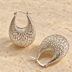 May include: A pair of silver hoop earrings featuring a U-shaped silhouette with an openwork lattice or grid pattern. The earrings have a polished metallic finish and include a hinged post closure mechanism at the top of each hoop.