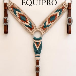 May include: A macrame breast collar with the text EQUIPRO, featuring beige, teal, and rust-colored cord patterns. It includes brown leather straps, silver-toned metal rings, and ornate silver buckles at the connection points for equestrian gear.