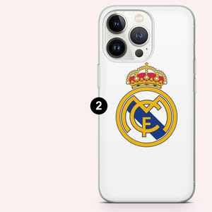 Puede incluir: Funda de tel&eacute;fono blanca con el logo del Real Madrid. El logo incluye un c&iacute;rculo dorado con las letras "MCF", una franja azul y una corona. La funda tiene un dise&ntilde;o transparente y protector.