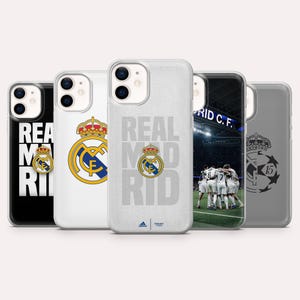 Puede incluir: Cinco fundas para tel&eacute;fono con dise&ntilde;os del Real Madrid. Las fundas muestran el logotipo del equipo, las palabras "REAL MADRID" y una escena del estadio. Las fundas son de color negro, blanco y gris. Tambi&eacute;n se ve el logotipo de Adidas.