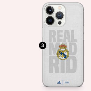 Puede incluir: Una funda blanca para tel&eacute;fono con las palabras "REAL MADRID" en gris, con el escudo del equipo en el centro. La funda tambi&eacute;n presenta los logotipos de Adidas y Emirates Fly Better en la parte inferior.