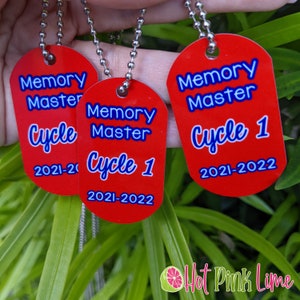 May include: Three red metal dog tags with blue text that reads "Memory Master Cycle 1 2021-2022". The tags are attached to silver chains.