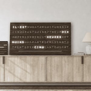 Peut inclure: Trois horloges à mots rectangulaires avec des cadres en bois sombre et du texte français illuminé en blanc. La grande horloge centrale affiche les mots IL EST, DIX, HEURES, MOINS et CINQ en lumière blanche sur un fond de lettres sombres.