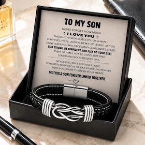 May include: A black leather bracelet with a silver knot design, presented in a black gift box. The box contains a printed message that reads "TO MY SON" and a heartfelt message from a mother to her son.