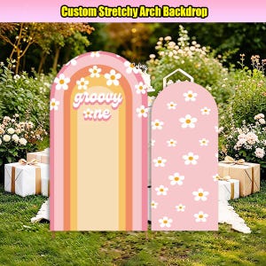 May include: Two arched fabric backdrops with a stretchy finish. The larger arch features a rainbow pattern in shades of pink, orange, and yellow with white daisy flowers and the text "groovy one". The smaller arch is pink with white daisies.