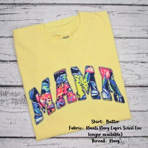 May include: A yellow t-shirt with the word "MAMA" in colorful, patterned letters. The shirt is made of butter-colored fabric and features a navy thread. The fabric is Nauti Navy Capri Soleil.