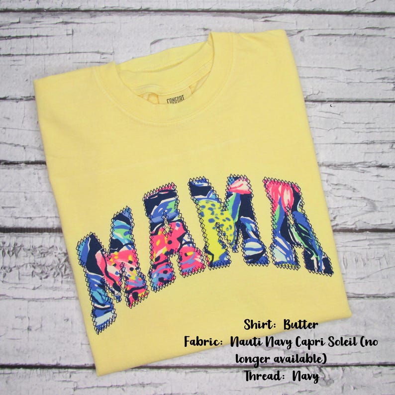 May include: A yellow t-shirt with the word "MAMA" in colorful, patterned letters. The shirt is made of butter-colored fabric and features a navy thread. The fabric is Nauti Navy Capri Soleil.