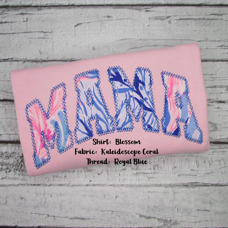 May include: A light pink shirt with the word "MAMA" embroidered in large letters. The letters are filled with a blue and white floral pattern and outlined with blue stitching. The shirt's fabric is Kaleidoscope Coral.