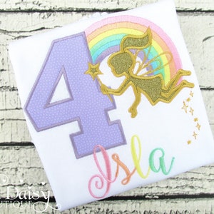May include: White t-shirt with a large number 4 in lavender, a rainbow, and a gold fairy holding a star wand. The name "Isla" is written in colorful script. The shirt is designed for a child's birthday.