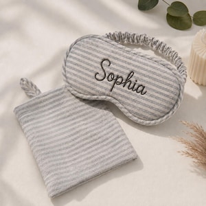 Può includere: Una mascherina per dormire a righe grigie e bianche con il nome Sophia ricamato in filo scuro, dotata di fascia elastica, abbinata a una pochette rettangolare coordinata in tessuto a righe grigie e bianche con una piccola linguetta.