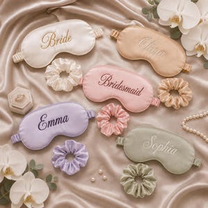 May include: A collection of five satin sleep masks and five matching scrunchies in white, champagne, pink, lavender, and sage green. Each mask features embroidered text including Bride, Olivia, Bridesmaid, Emma, and Sophia. A ring box is included.