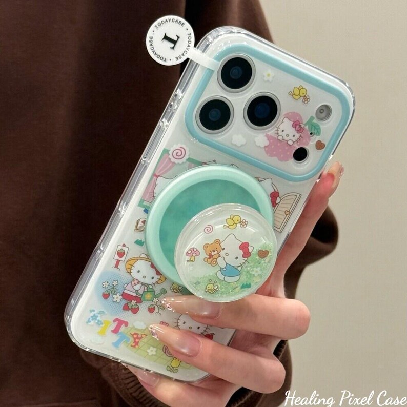Puede incluir: Funda transparente para tel&eacute;fono con borde azul claro y un pop socket. La funda presenta un dise&ntilde;o de Hello Kitty con flores y otros gr&aacute;ficos. El pop socket es de color verde claro y tiene un dise&ntilde;o de Hello Kitty.