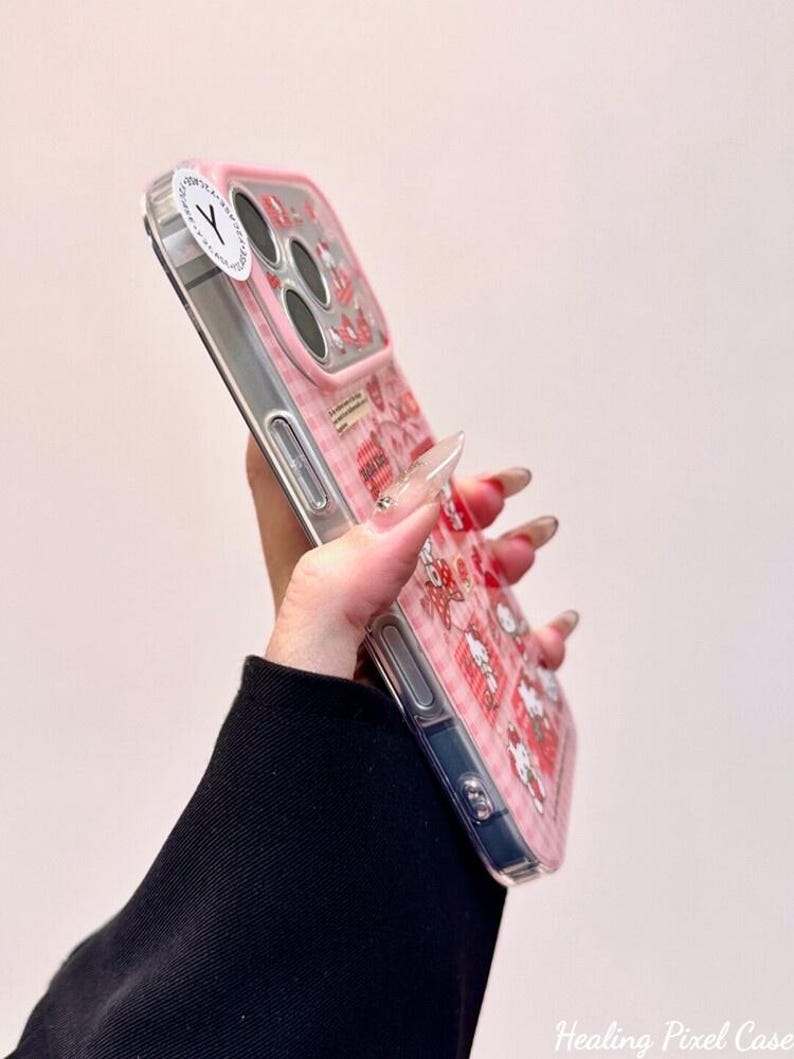 K&ouml;nnte beinhalten: Eine transparente Smartphone-H&uuml;lle mit rosa-wei&szlig;em Karomuster, kleinen Cartoon-Figuren und roten Herz-Symbolen. Die H&uuml;lle verf&uuml;gt &uuml;ber einen erh&ouml;hten rosa Kameraschutz und einen runden wei&szlig;en Aufkleber mit einem schwarzen Y-Symbol in der oberen Ecke.