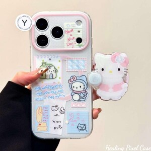 May include: A clear phone case with a pink camera frame, decorated with various stickers including Hello Kitty characters, hearts, and text that reads "Have a Nice Day" and "The Milkyway is hot-you are the ideal of the world". Includes a Hello Kitty phone grip.