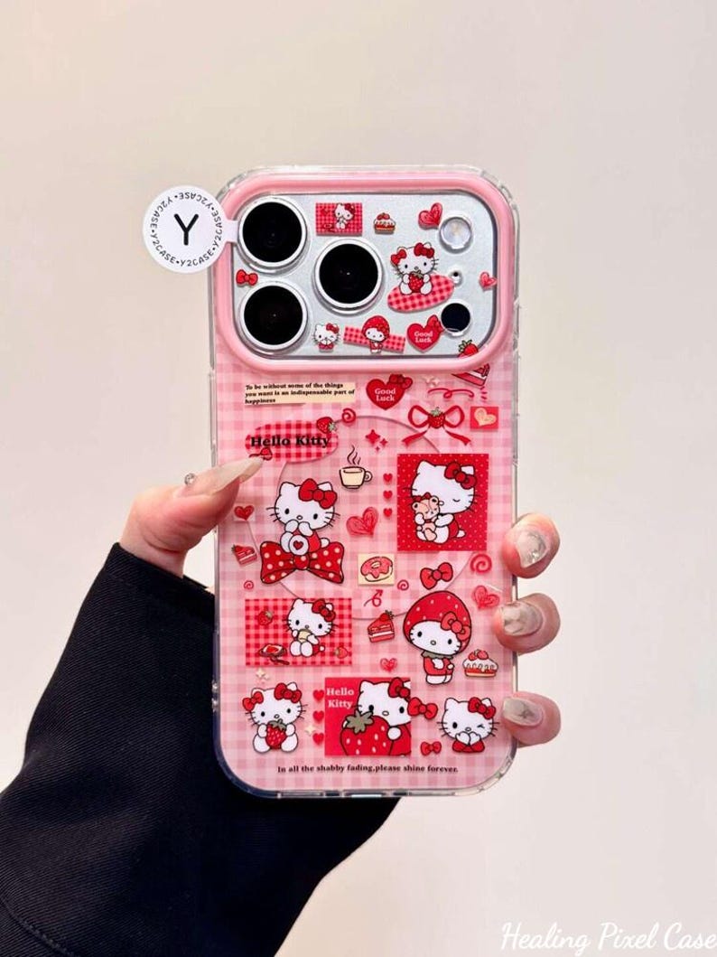 K&ouml;nnte beinhalten: Eine transparente Handyh&uuml;lle mit rosafarbenem Karomuster und zahlreichen Hello Kitty-Grafiken in Rot und Wei&szlig;. Das Design umfasst Erdbeeren, Herzen und kleine Textelemente. Ein rundes wei&szlig;es Etikett mit einem schwarzen Y-Logo ist oben befestigt.