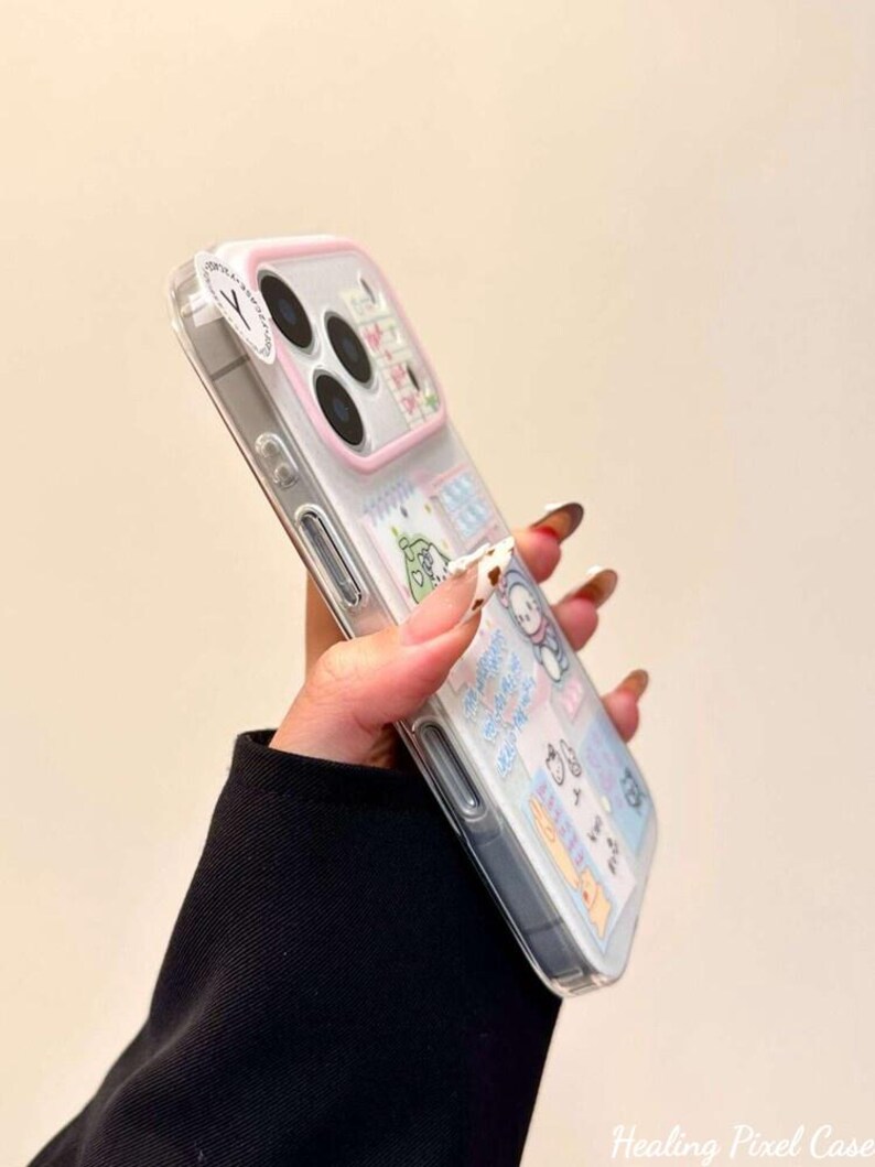 May include: A clear smartphone case with a light pink camera frame and a collage of various cartoon character stickers and blue text accents. The case features a transparent back panel that displays the phone's design underneath the decorative stickers.