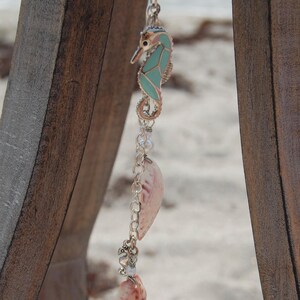 May include: A decorative hanging ornament featuring a silver-toned seahorse charm with light blue enamel inlay, connected by a silver chain to two natural seashells and small white beads, creating a vertical arrangement of coastal-themed elements.
