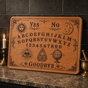 May include: A rectangular wooden spirit board featuring laser-engraved black designs including the alphabet, numbers 0-9, the words YES, NO, and GOODBYE, a sun, a moon, an all-seeing eye, a planchette, and a globe, with ornate corner flourishes.