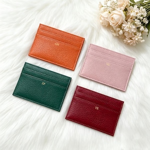 May include: Four leather cardholders in orange, pink, green, and burgundy. Each cardholder has a textured surface and gold initials. The orange cardholder has "GH", the pink has "NK", the green has "ZP", and the burgundy has "TE".